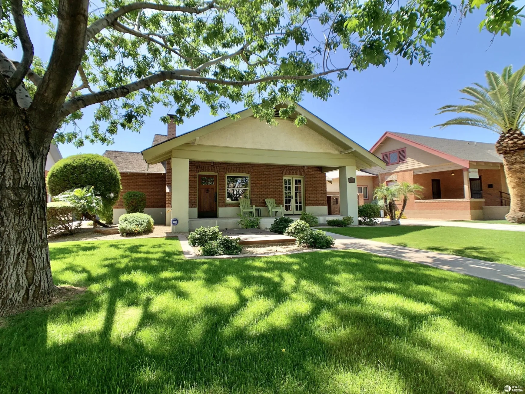 Brick and stucco bungalow with porch shaded by mature trees