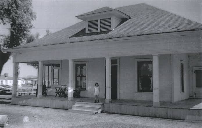 Archival black-and-white photograph of a broad-porch house with a child at the front steps